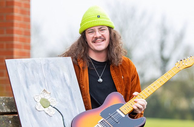 John Hancock holding a guitar and his painting of a flower