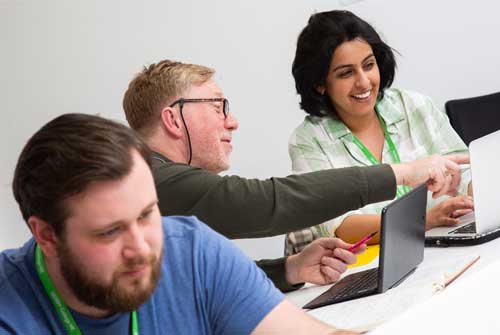 Three adult learners working at desks with laptops