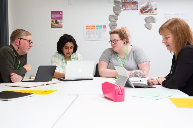 Four mature Teacher Training students sat around a table talking to one another.