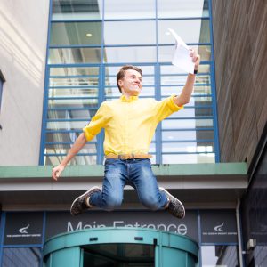 A-level student jumping in the air holding his results.