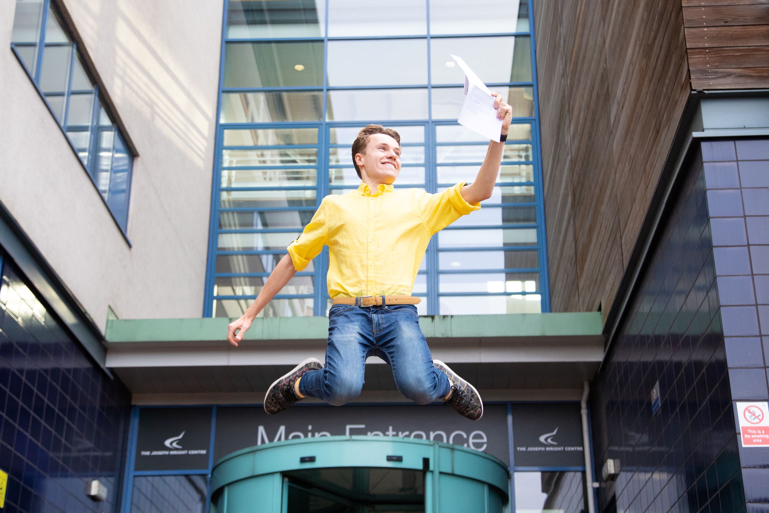 A-level student jumping in the air holding his results.