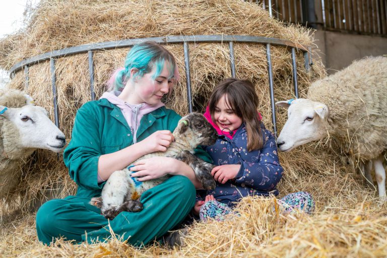 Agriculture student tending to a lamb with a child at Broomfield Hall's Lambing Sunday.