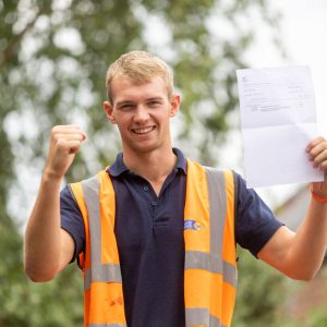 Elliott Poplar holding his T Level results celebrating, wearing a hi-vis vest.