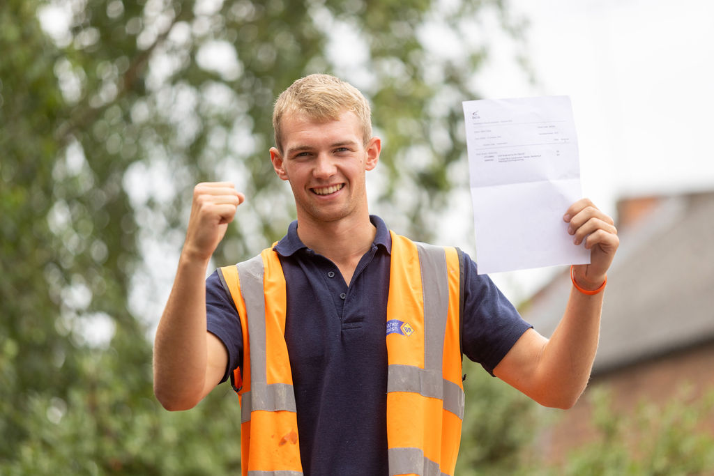 Elliott Poplar holding his T Level results celebrating, wearing a hi-vis vest.