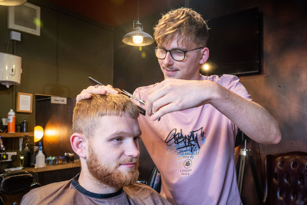 Male barber giving a male client with a beard a haircut.