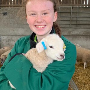 Female student wearing green overalls holding a lamb.