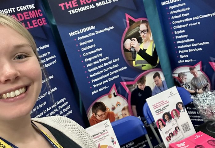 Schools Liaison Officer Taylor Marcer-McCan smiling infront of a desk with marketing material and colourful banners.