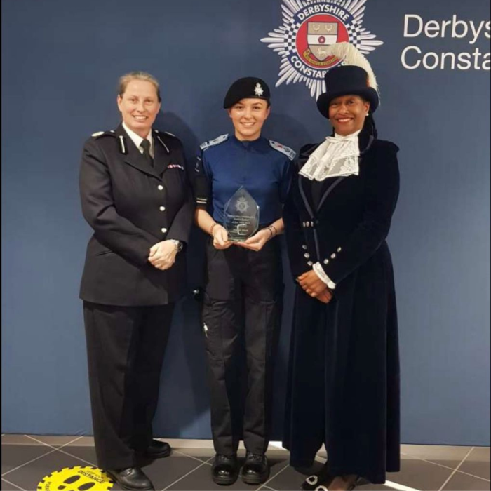 Female public service student holding a certificate stood by a female police officer and the High Sherrif of Derbyshire.