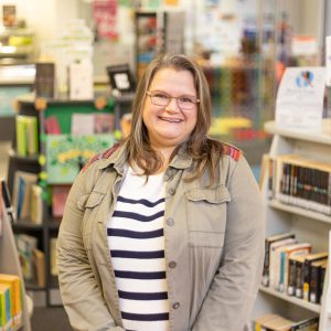 Lady with glasses and shoulder length hair in a library.