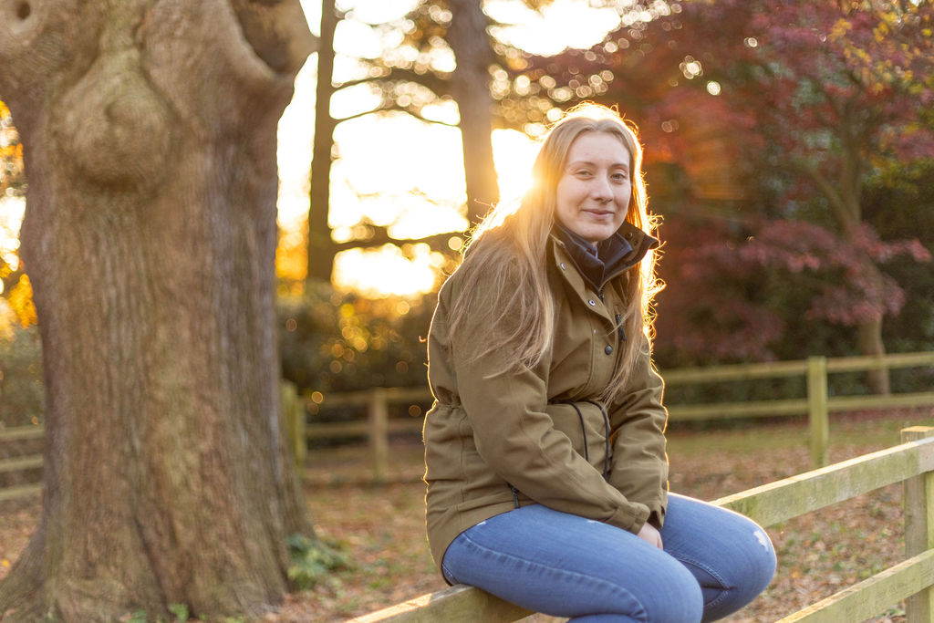 Young lady sat on a wooden fence by a tree.