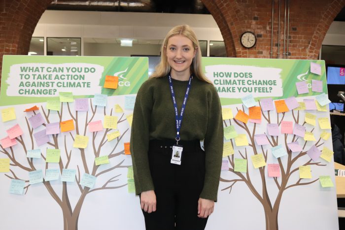 Young woman with blonde hair stood between two boards with trees and sticky notes on them.