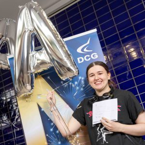 Young female with brown hair holding a baloon and a document with exam results.