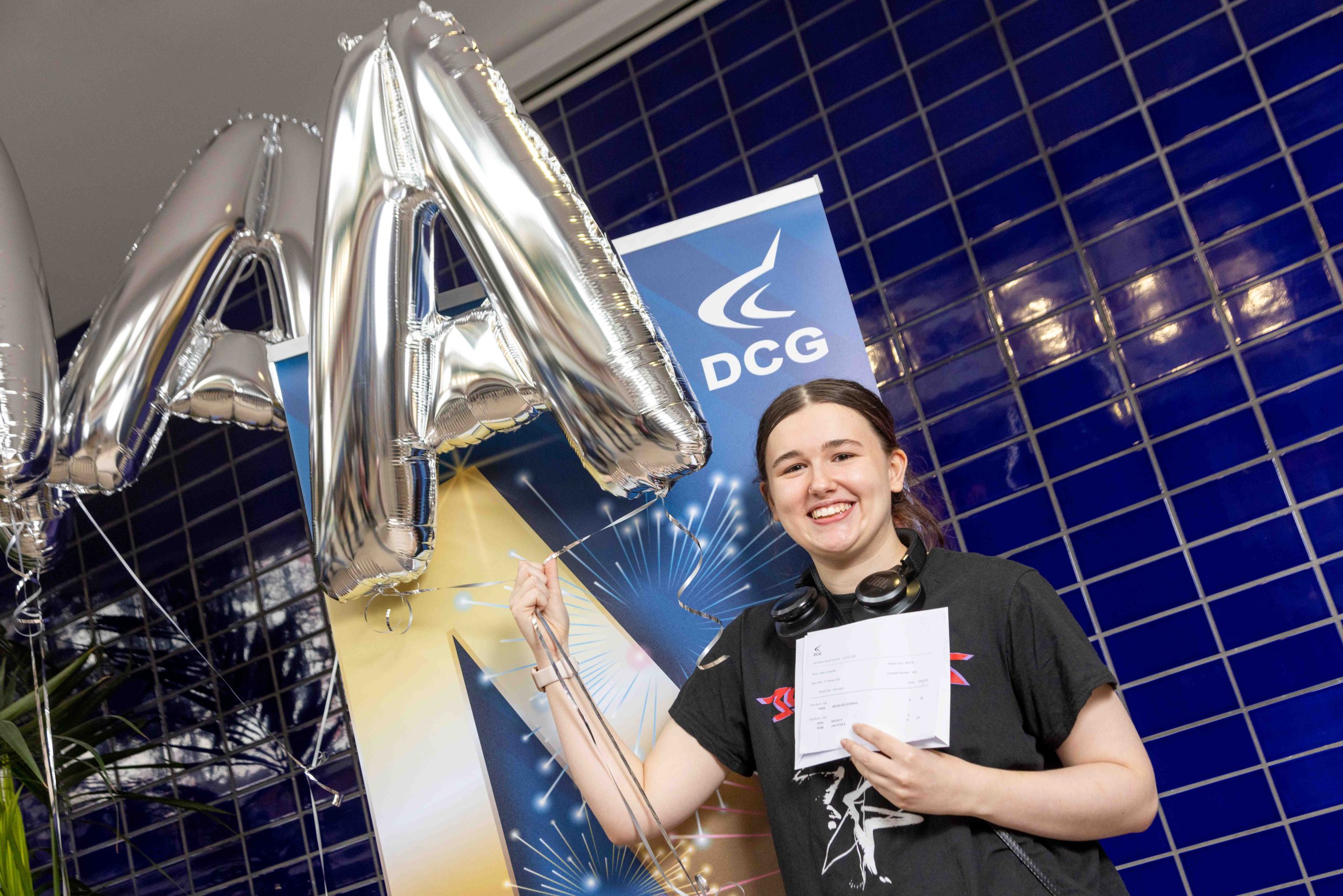 Young female with brown hair holding a baloon and a document with exam results.