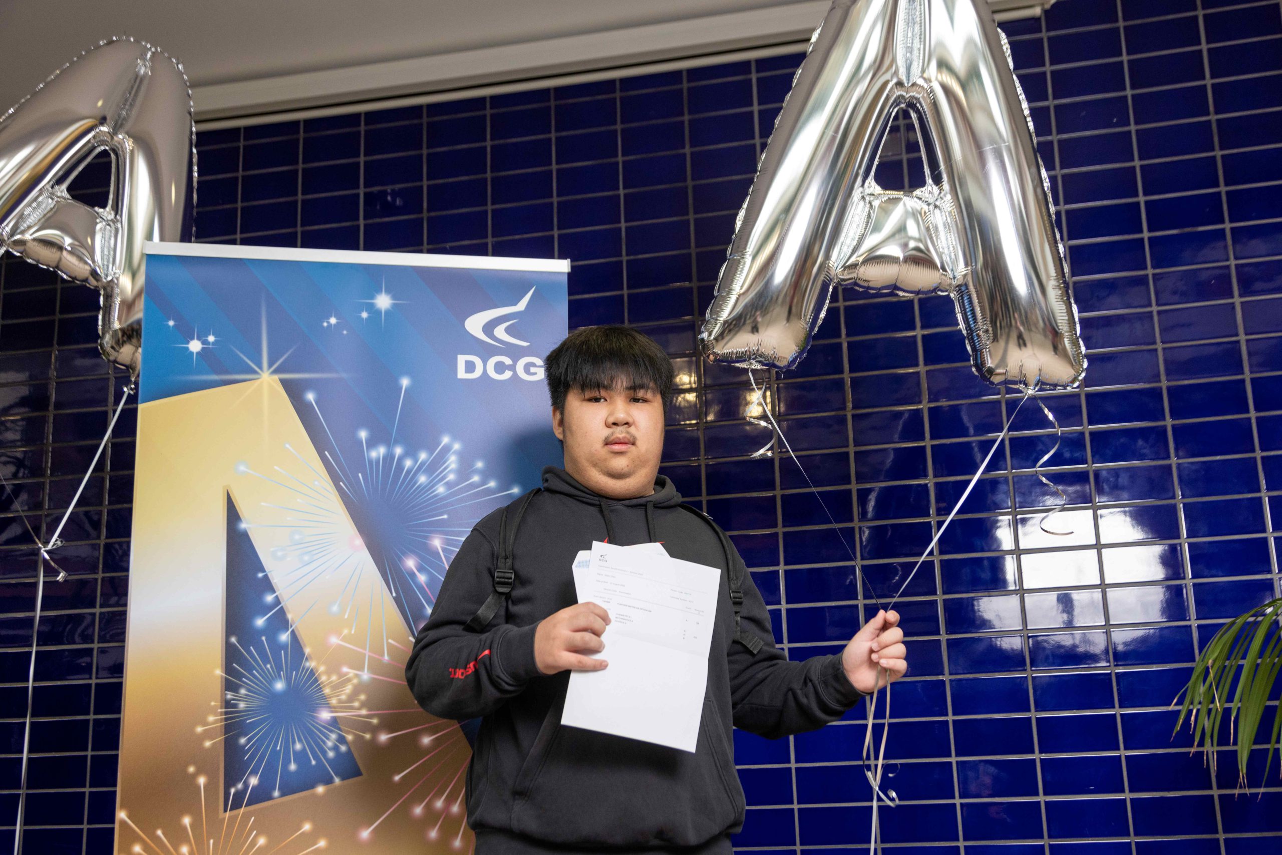 Male student eith black hair holding a document with exam results.