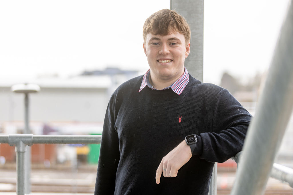 Young male wearing a black sweater, leaning against a white pillar.