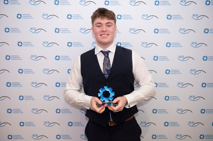 Young male wearing a suit holding an award infront of a white background.