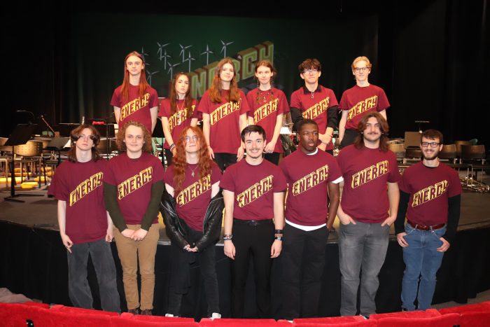 A group of Derby College students stood infront of a large stage wearing purple shirts that read 'Sinfonia'