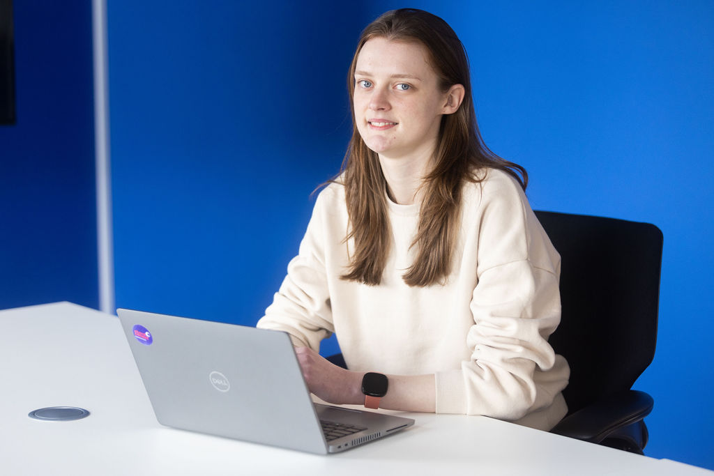 Young female engineer with brown hair and a white jumper sat typing on a laptop.