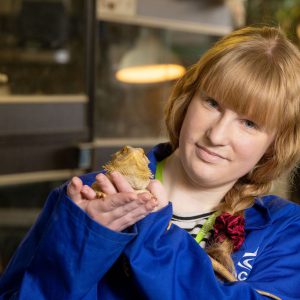 Celine Frosthagen, a student with brown hair wearing a blue coat holding a frog.