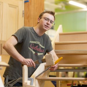 Young male with black hair and glasses doing joinery.