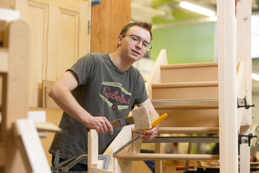 Young male with black hair and glasses doing joinery.