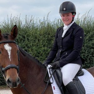 Libby Dodes, a young female wearing riding gear whilst riding a brown horse.