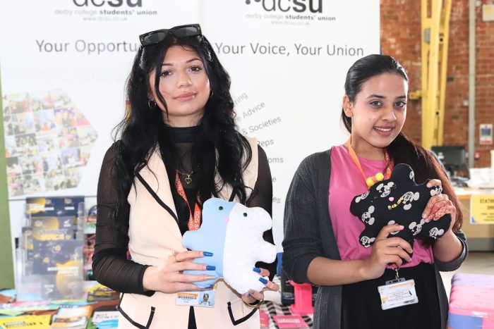 Two business students holding some of their 'Cuzzy Bears' up in the air.