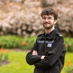 Former DCG Public Services students Harry Sherwin with his arms crossed, wearing his police uniform.
