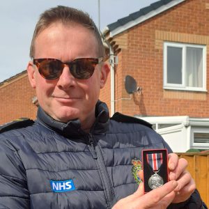 Construction teacher Michael Grange wearing sunglasses and a black gilet, holding his King's Coronation Medal