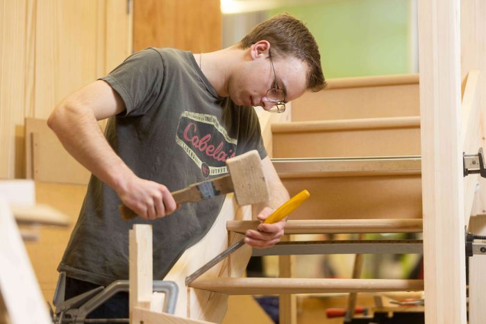 Apprentice Kai working on his woodwork project using a hammer and chisel.