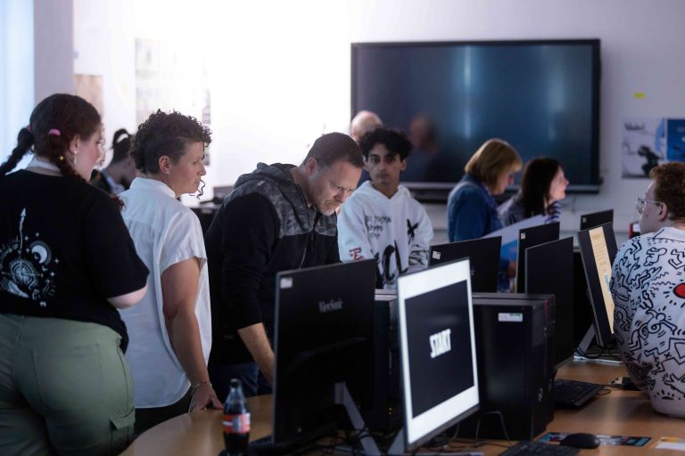 People stood around a table of computers, looking at the monitors.