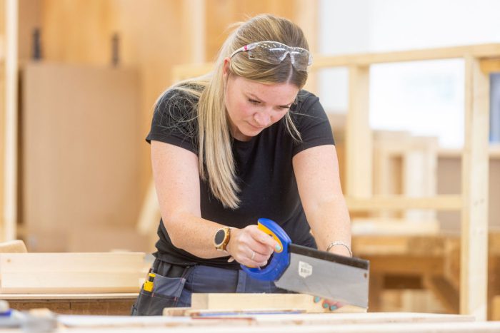 Female adult learner Kim Gill sawing a piece of wood.
