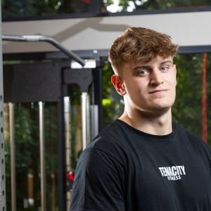 Young man stood by a weights machine.
