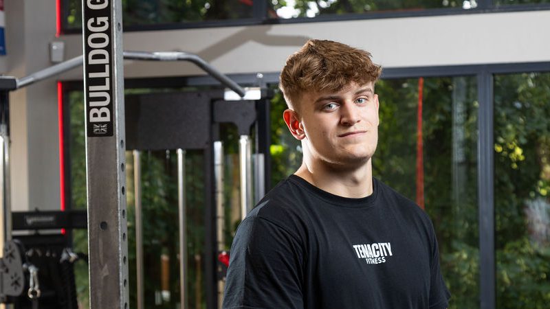 Young man stood by a weights machine.