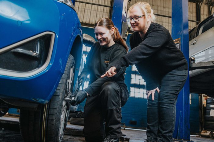 Two young ladies doing work on a car tyre.