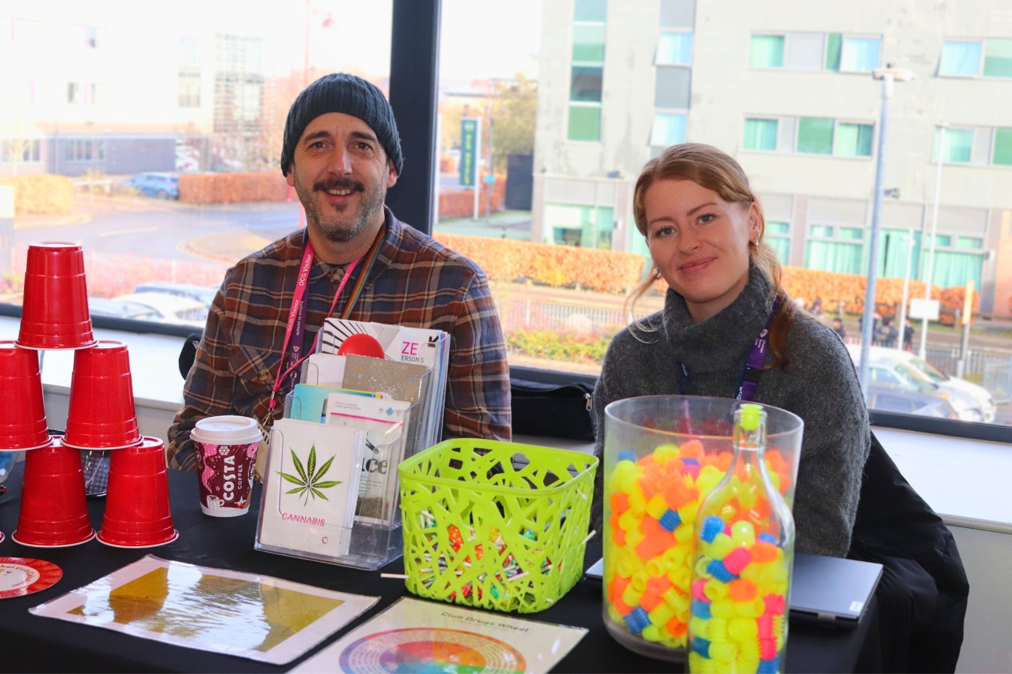 Two people wearing lanyards sat at a stall with a display.