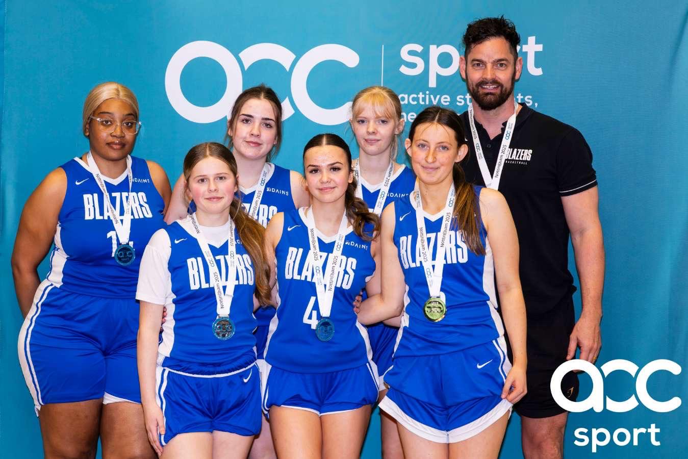 A team of basketball players and their coach wearing silver medals.