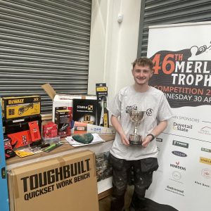 Young carpentry apprentice holding a trophy stood by tools.