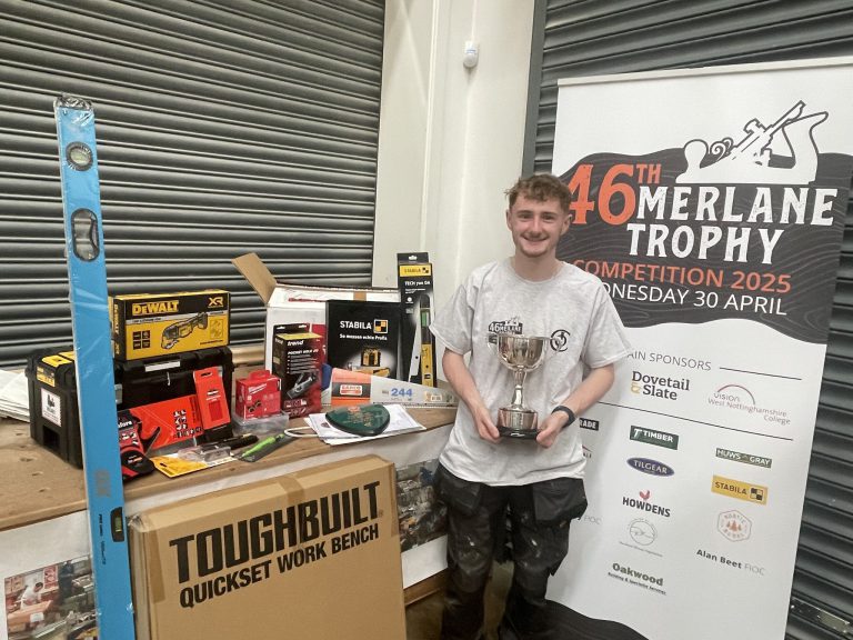 Young carpentry apprentice holding a trophy stood by tools.
