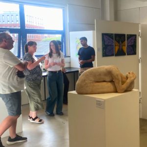An audience gathered looking at pieces of art at an exhibition.