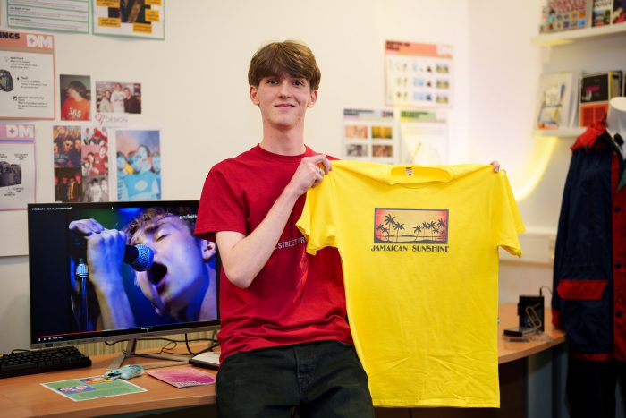 Young student holding a yellow t-shirt he has designed.