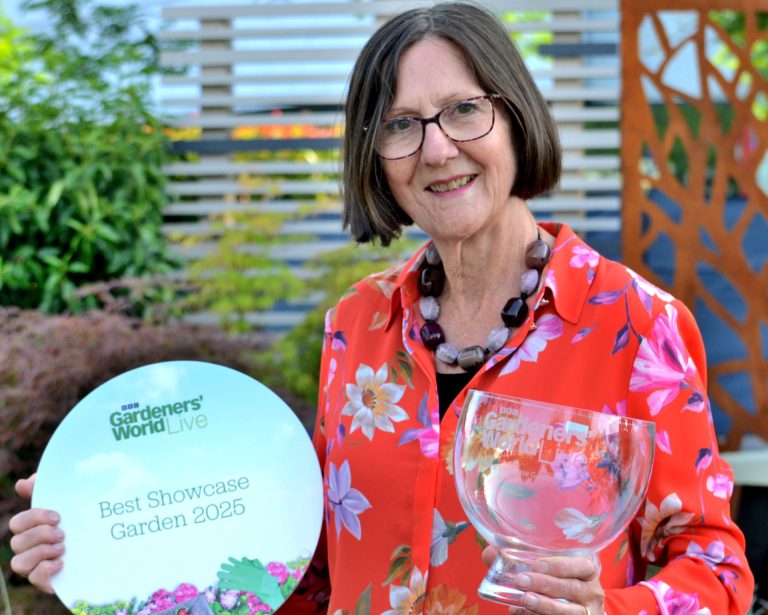 Lady wearing a red floral shirt holding a plate and an award