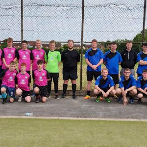 Two football teams stood in one big group, one wearing blue jerseys, one wearing pink jerseys
