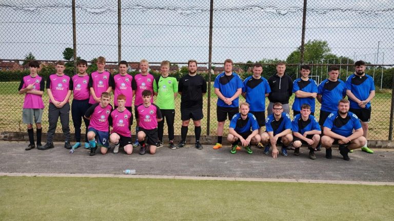 Two football teams stood in one big group, one wearing blue jerseys, one wearing pink jerseys