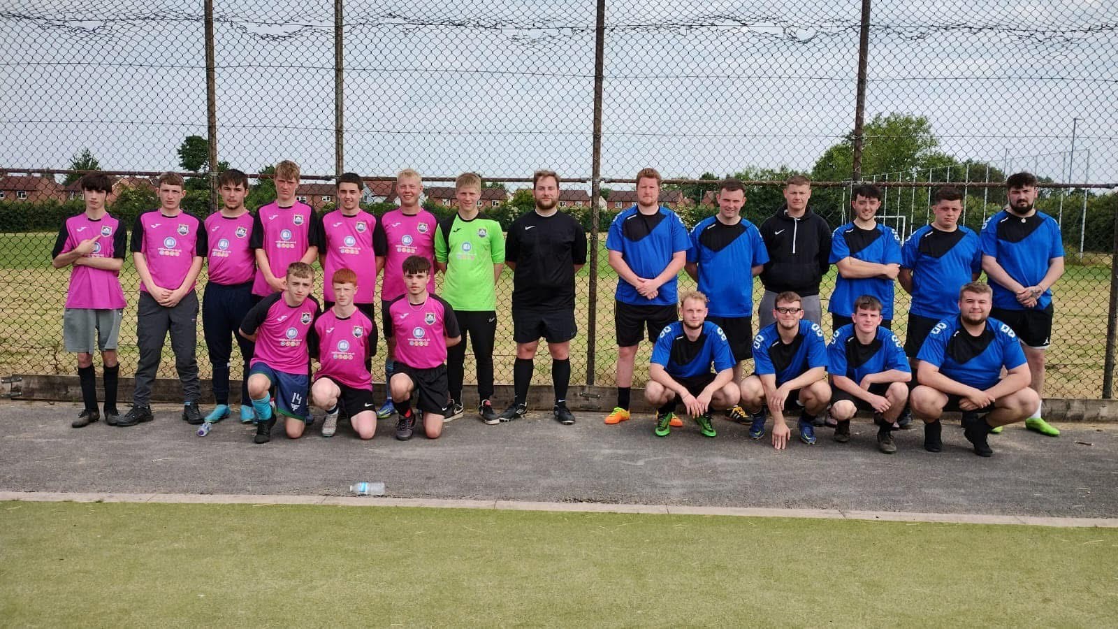 Two football teams stood in one big group, one wearing blue jerseys, one wearing pink jerseys
