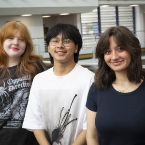 Three young students stood by a bannister.
