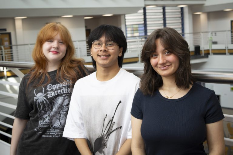 Three young students stood by a bannister.