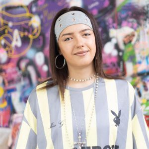 Art student Liana, a young student wearing a blue and white striped shirt and a blue bandana.