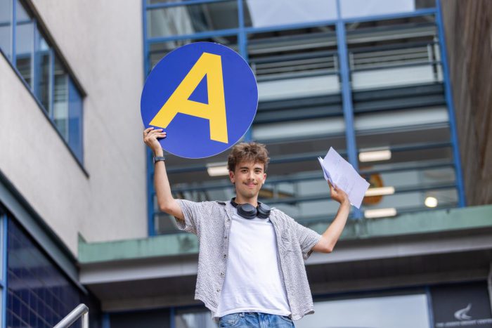 Young student holding a card with an A written on it on A-level results day