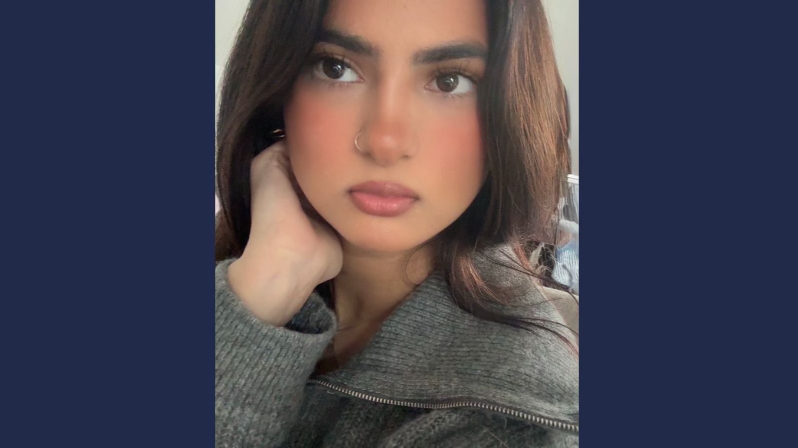 Person wearing a grey zip-up sweater inside with soft furnishings visible in the background.